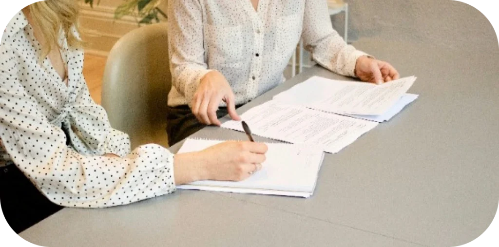 two ladies sit at a table and sign paperwork