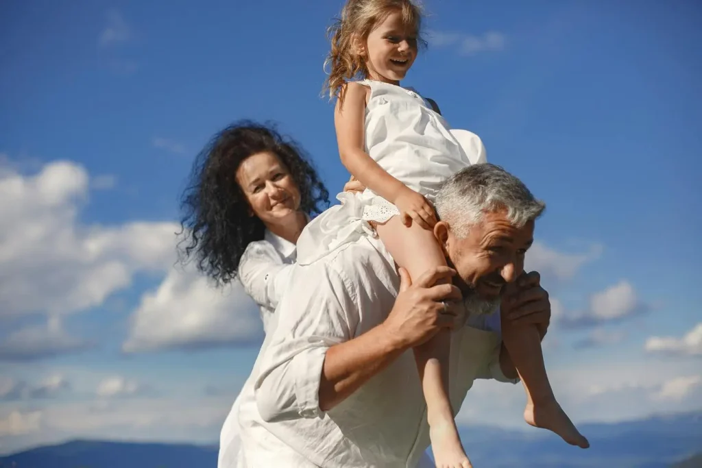 A mom and a dad play with their adoptive kid who is being carried by her father